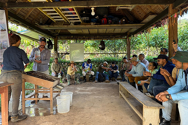 A group of people sitting under a hut. Two people demonstrating an experiment. 