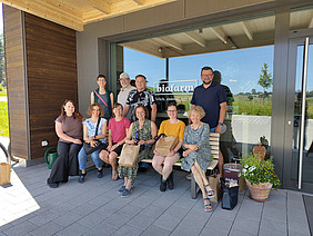 Gruppenbild: 10 Personen sitzen und stehen vor einer Scheibe mit einer "Biofarm" Beschriftung.