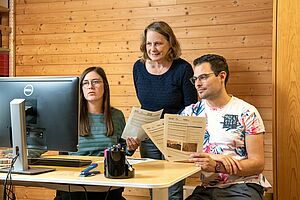 Three employees at the computer with fact sheets in their hands.