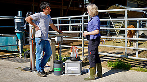 Two people stand in front of a scientific measuring device at the cattle shed and discuss.