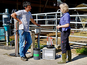 Two people stand in front of a scientific measuring device at the cattle shed and discuss.