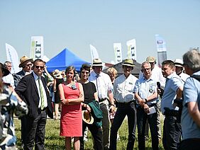 Eine Gruppe von Menschen auf einer Wiese mit Zelten und Bannern im Hintergrund