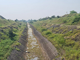 Ausgetrockneter Wasserkanal in grüner Landschaft.