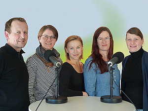 Fünf Personen an einem Tisch an Mikrofonen.