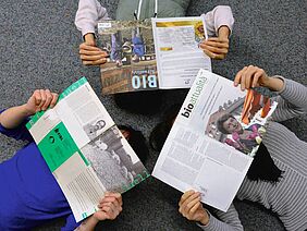 Drei Personen liegen am Boden und lesen in verschiedenen Bioaktuell-Ausgaben aus drei Jahrzehnten