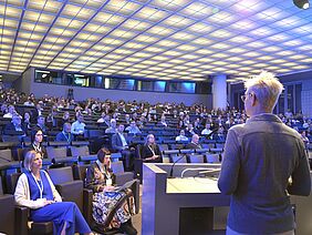 Ein Saal voll mit Menschen aus der Perspektive einer Sprecherin