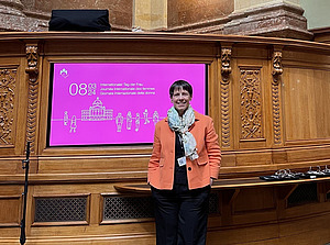 Zu sehen ist eine Frau vor einem pinkfarbenen Bildschirm, der auf den Internationalen Frauentag aufmerksam macht.
