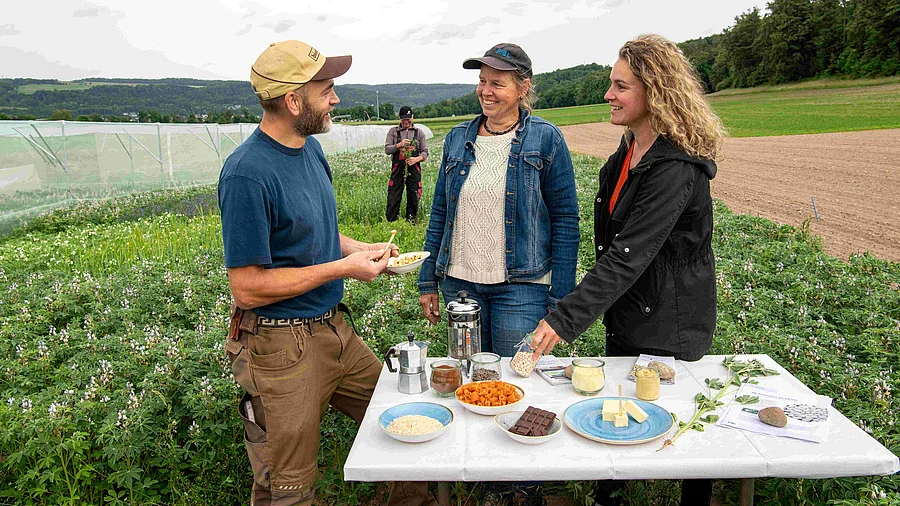 Un homme et deux femmes assis à une table dans un champ. 