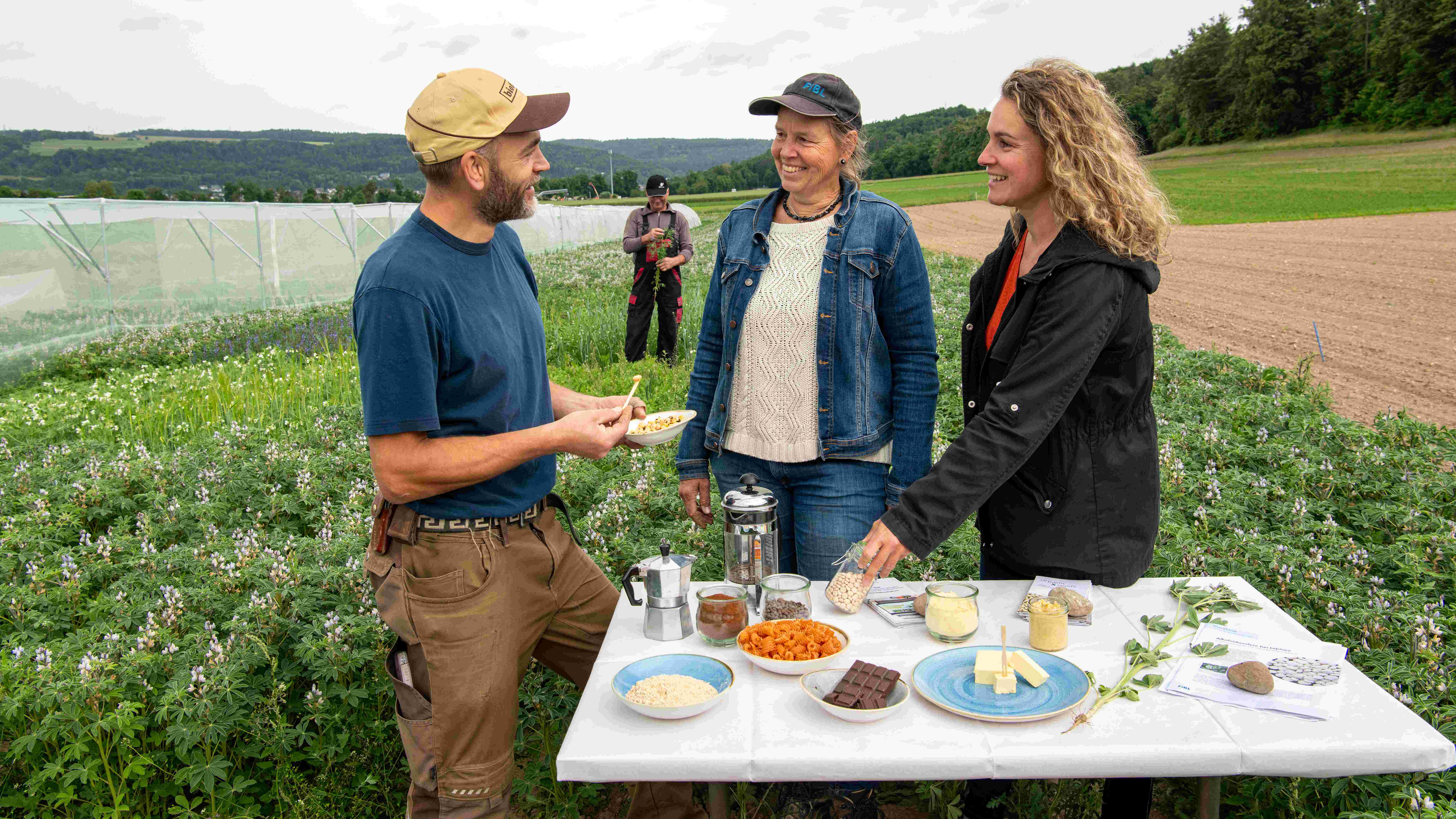 A man and two women sitting at a table in a field.