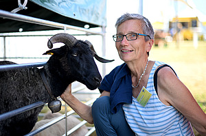 Frau streichelt eine schwarze Ziege.
