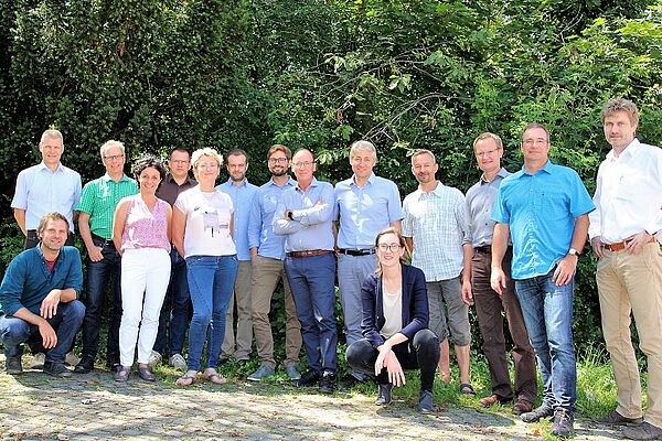 Eine Gruppe von Menschen vor Bäumen, davor zwei Personen in der Hocke.