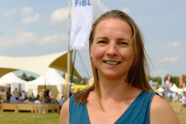 Frau schaut in die Kamera, dahinter Zelte einer Outdoor-Messe.