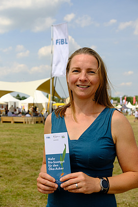 Frau schaut in die Kamera, dahinter Zelte einer Outdoor-Messe.