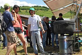 [Translate to Französisch:] Michael Scheifele demonstriert Biochar: Holzkohle produzieren, die gut für den Boden ist, und mit der Abwärme kochen.