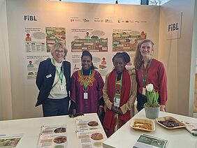 Vier Frauen an einem Stand lächeln für ein Foto.