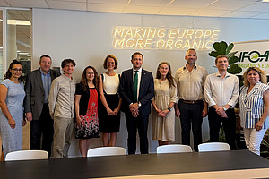 A group of people is standing in front of an illuminated sign that reads: “Making Europe More Organic.”