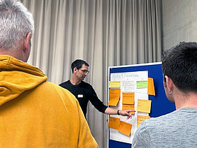 Mann zeigt etwas auf einer Tafel mit grossen Post-its.