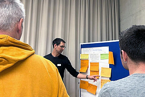 Mann zeigt etwas auf einer Tafel mit grossen Post-its.