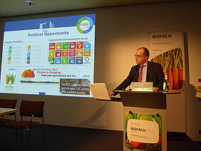 Man at a podium with a presentation in the background.