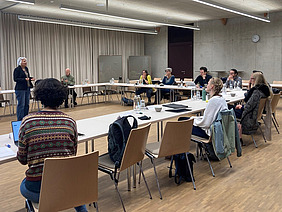 A woman talking to a group of people sitting in a room.