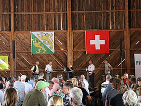 Podium in einem gut gefüllten Saal, auf der Bühne vier Männer und eine Frau in der Mitte als Leiterin.