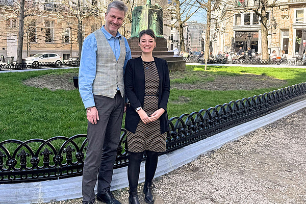 A man and a woman in front of a green space.