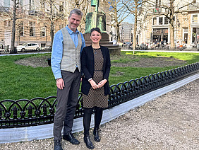 A man and a woman in front of a green space.