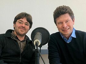 Two men behind a podcast microphone