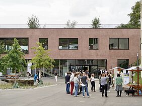 A reddish building with people and stalls in the square in front of it