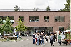 A reddish building with people and stalls in the square in front of it