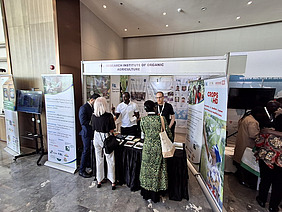 Two men at a stand with people gathering.