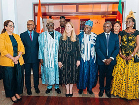 Nine men and women standing in front of a large door with Swiss and Cameroonian flags in the back.