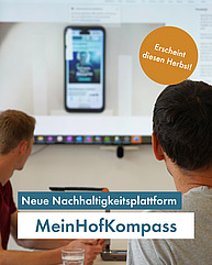 Zwei Männerköpfe mit kurzen Haaren sind von hinten zu sehen, wie sie auf einen grossen Bildschirm schauen. Auf diesem ist eine App zu sehen. Text "Neue Nachhaltigkeitsplattform: Mein HofKompass. Erscheint bald"