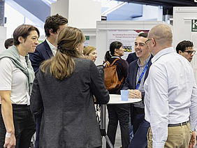 People standing at a desk, poster in the background.