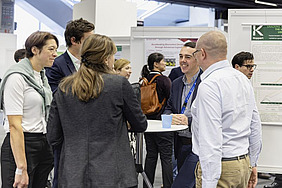 People standing at a desk, poster in the background.