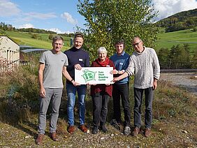 Quatre hommes et une femme sur fond vert tiennent un panneau avec le logo de la SPBC.