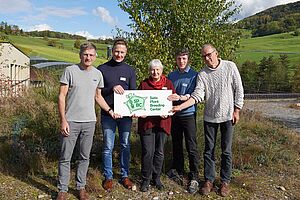 Vier Männer und eine Frau vor grünem Hintergrund halten ein Schild mit dem SPBC Logo.