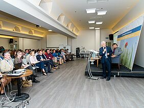 A man is speaking into a microphone, standing in front of an audience and looking at his presentation.